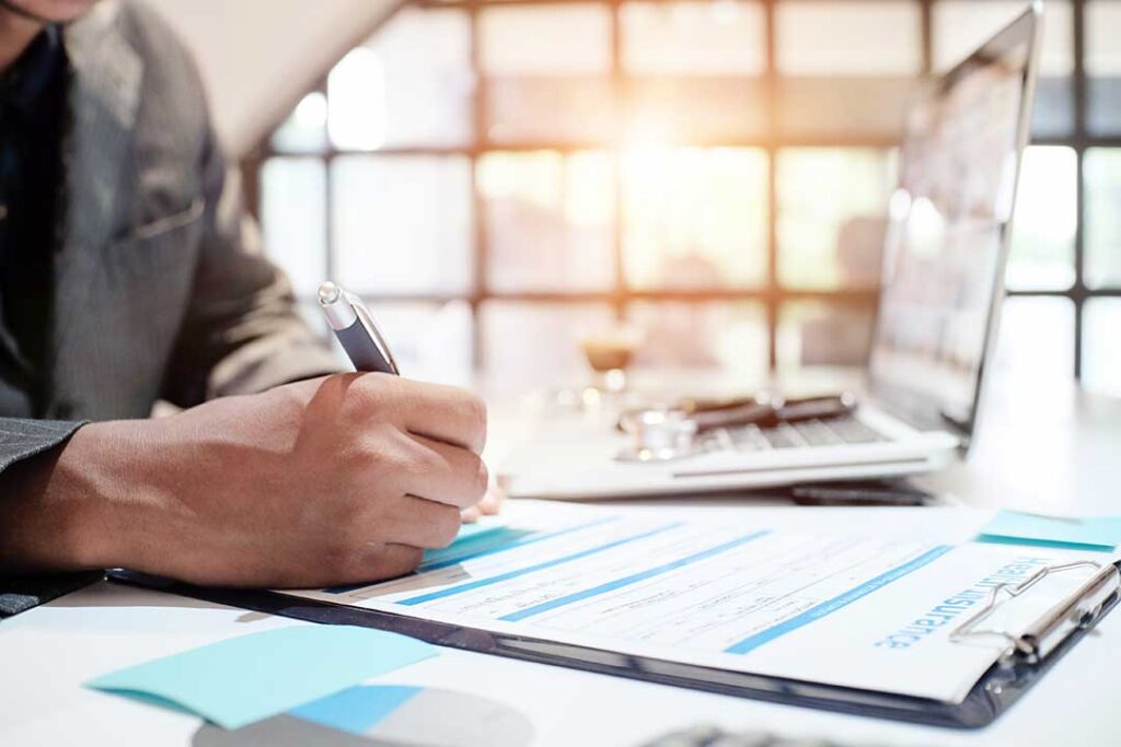 A person reviews an auto insurance policy and a car loan statement at a kitchen table.