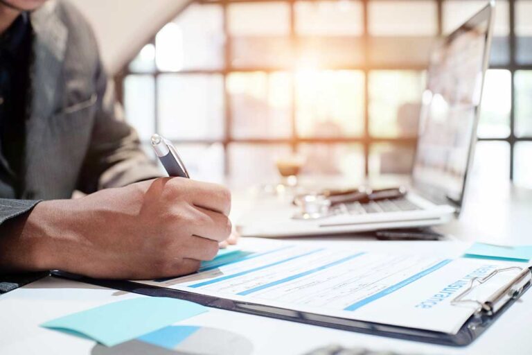 A person reviews an auto insurance policy and a car loan statement at a kitchen table.